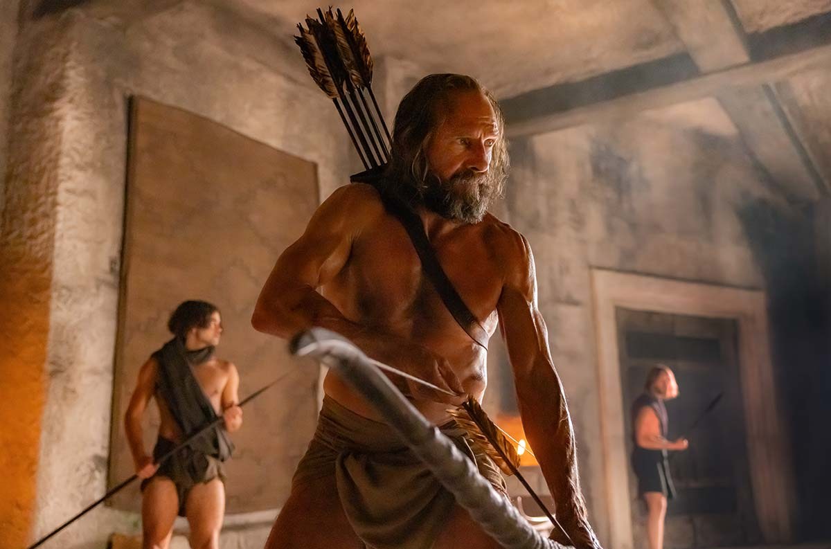 A shirtless Ralph Fiennes stringing a bow in The Return